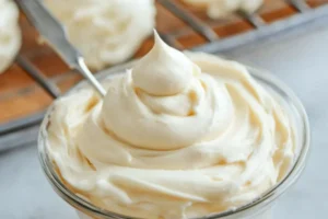 A bowl of smooth cream cheese frosting with a spatula

